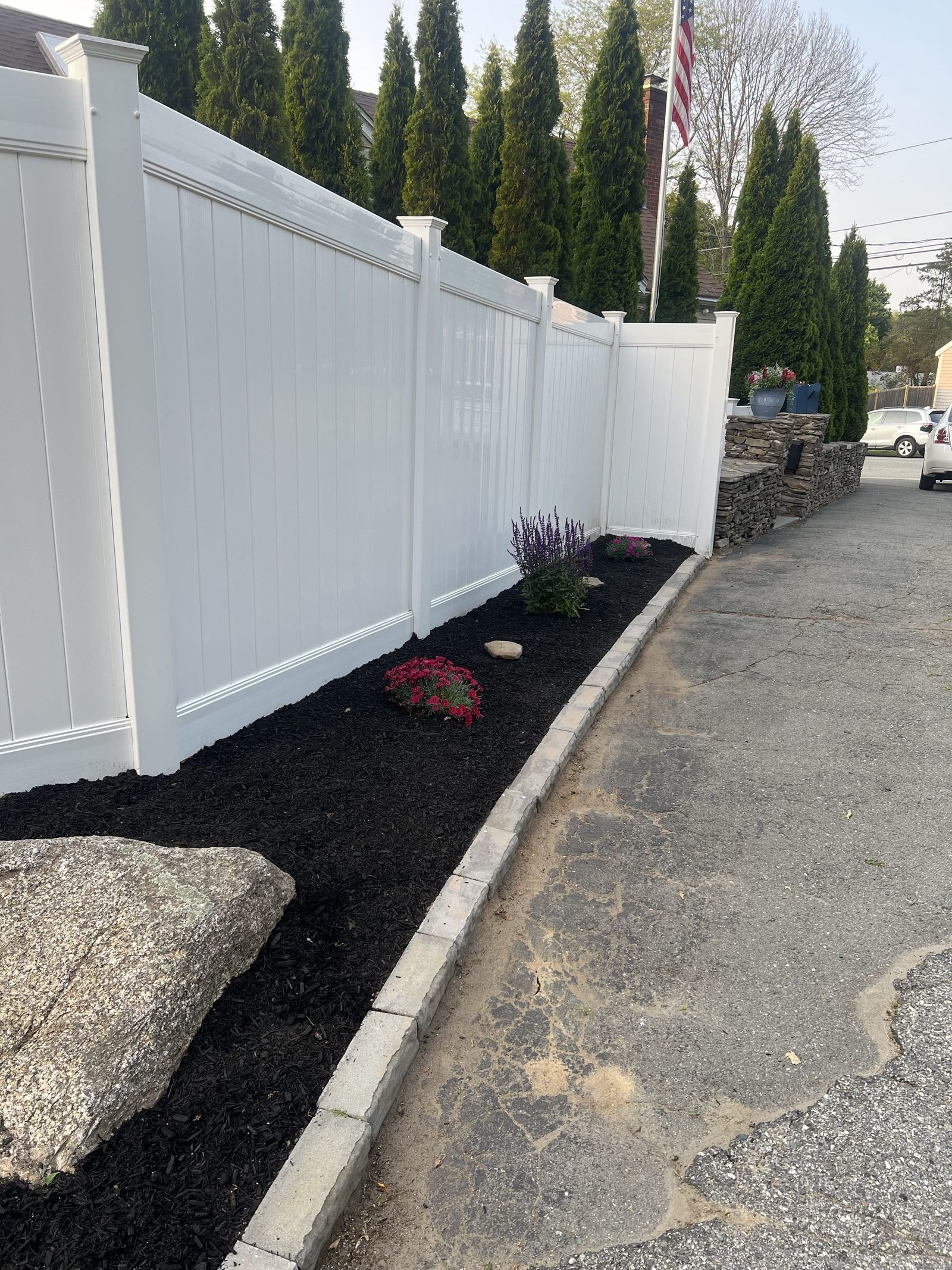 Fresh dark mulch bed with plantings along a white vinyl fence